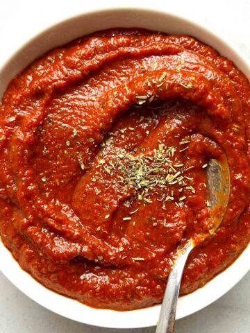 bowl of pizza sauce with dried herbs sprinkled on top and spoon in it.
