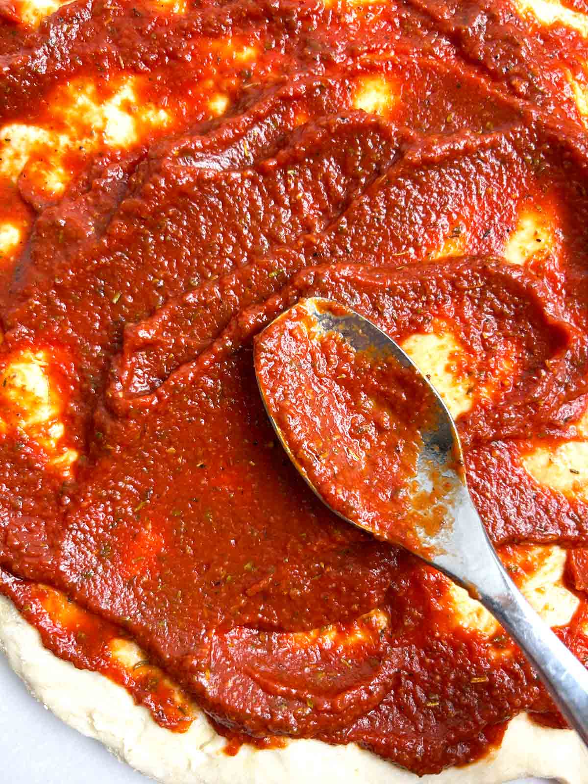 spoon spreading pizza sauce on dough.