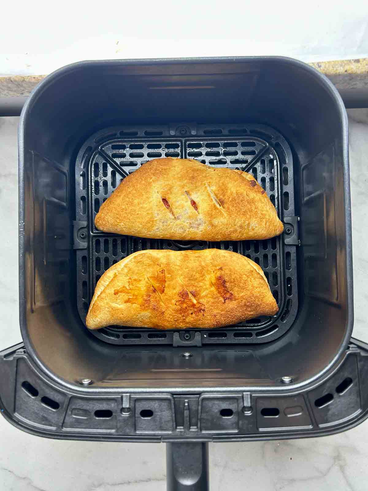 cooked calzones in air fryer basket.