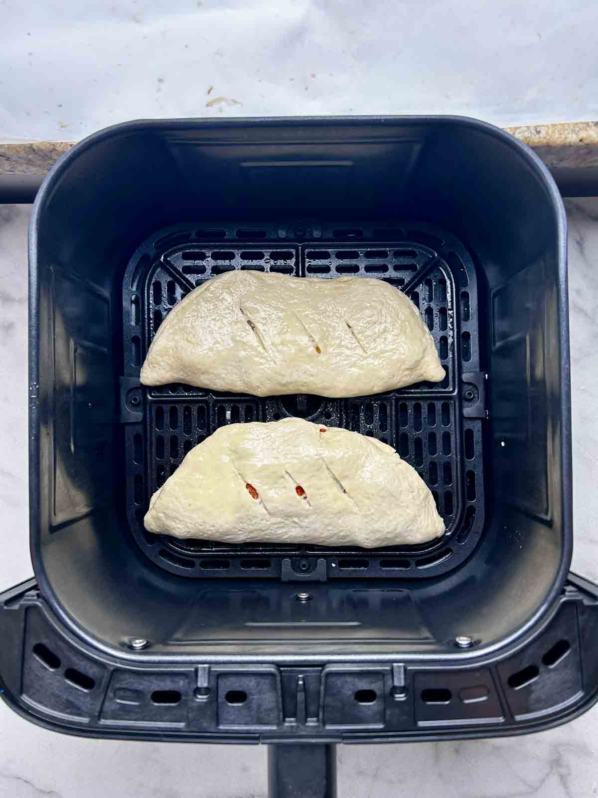 uncooked calzones in air fryer basket.