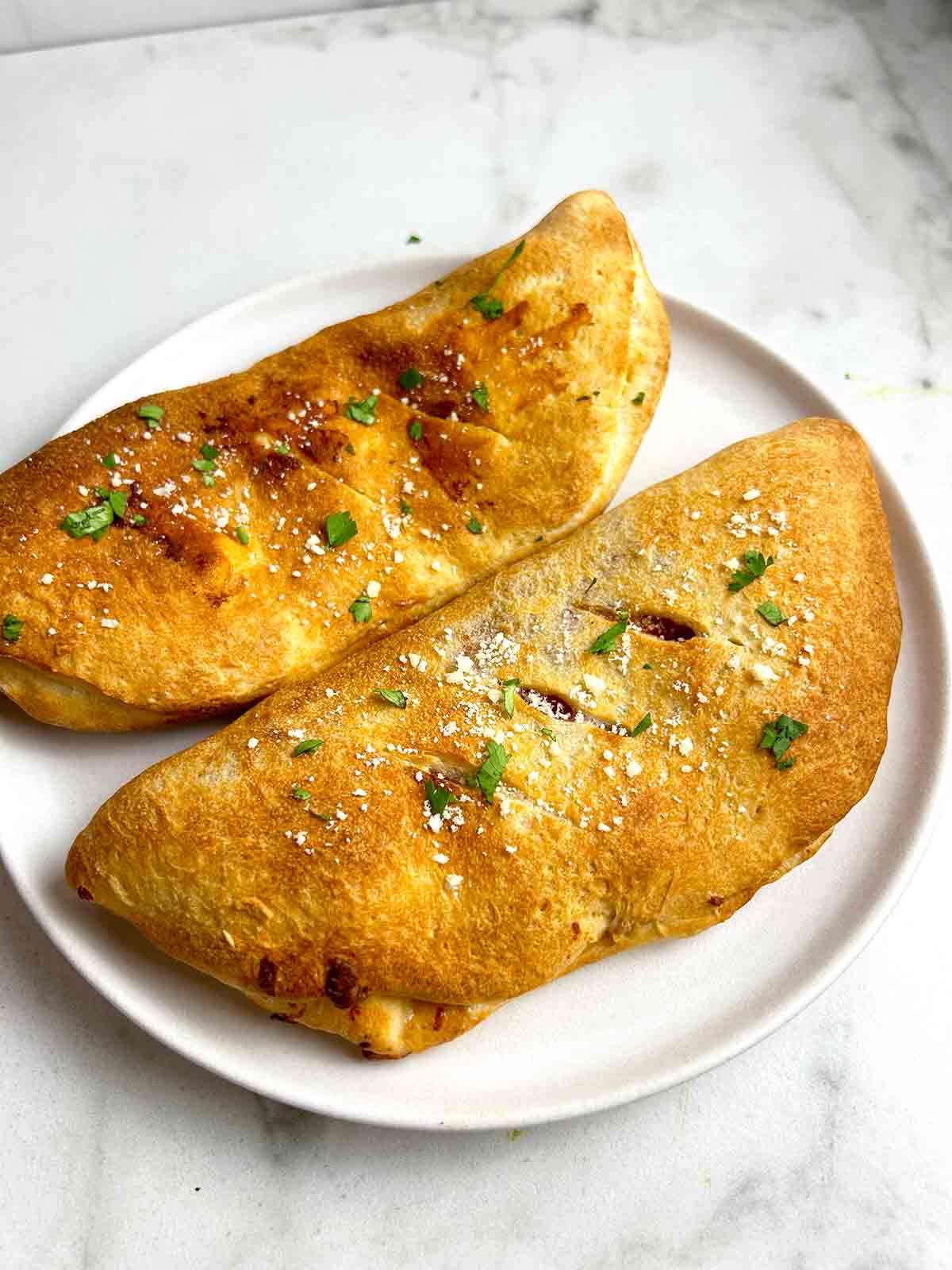 calzones on plate with parsley and parmesan sprinkled on top.
