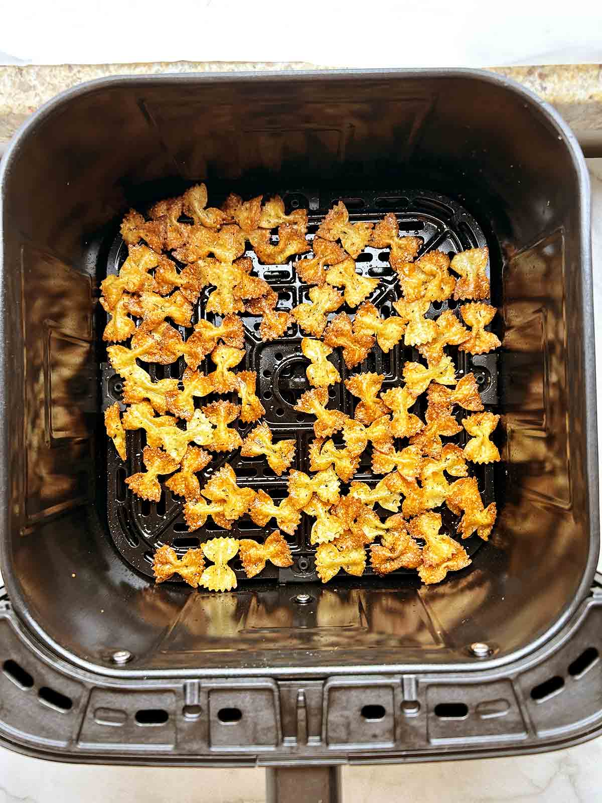 overhead shot of cooked pasta chips in air fryer basket.