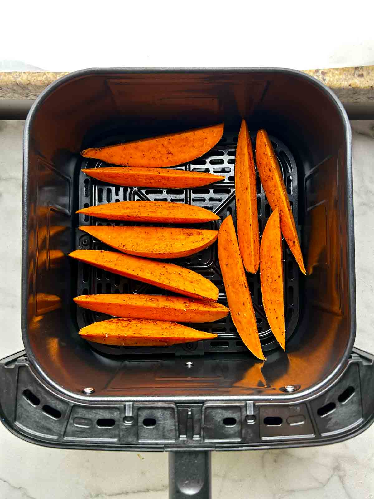sweet potato wedges arranged in air fryer basket.