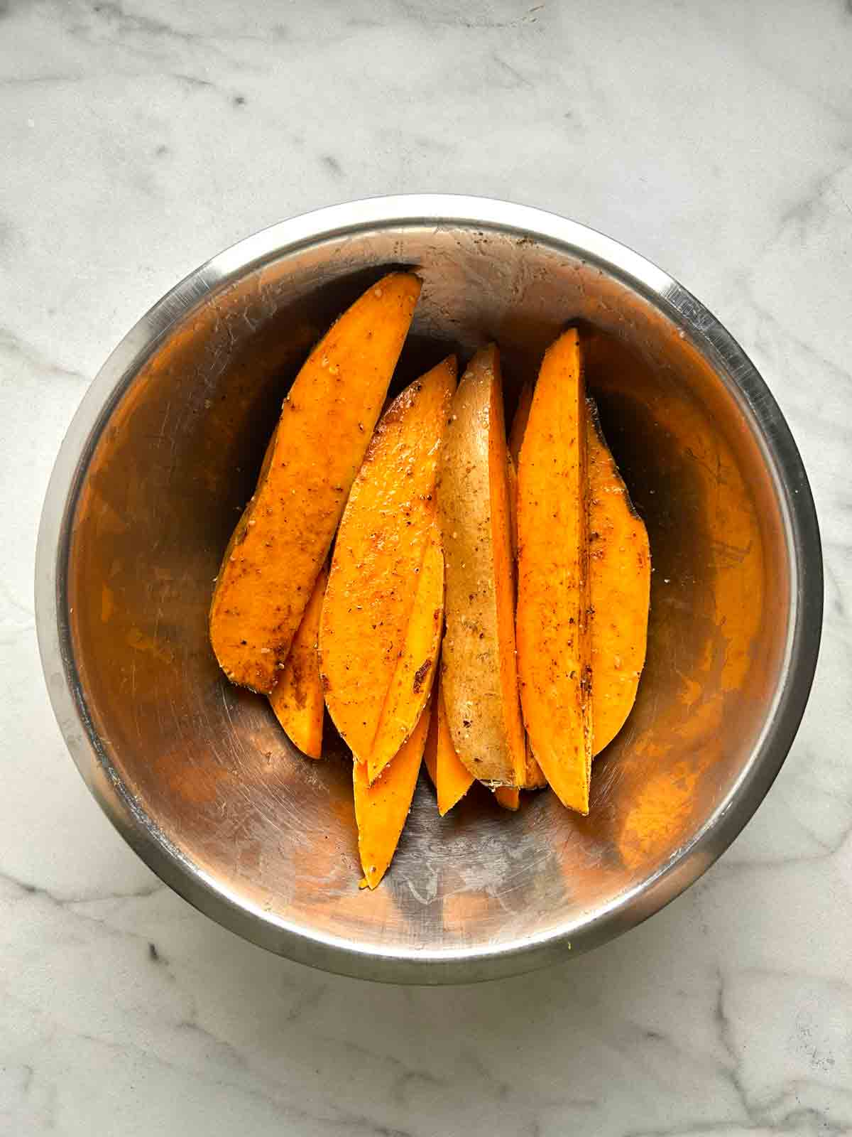 sweet potato wedges tossed with olive oil and spices in bowl.