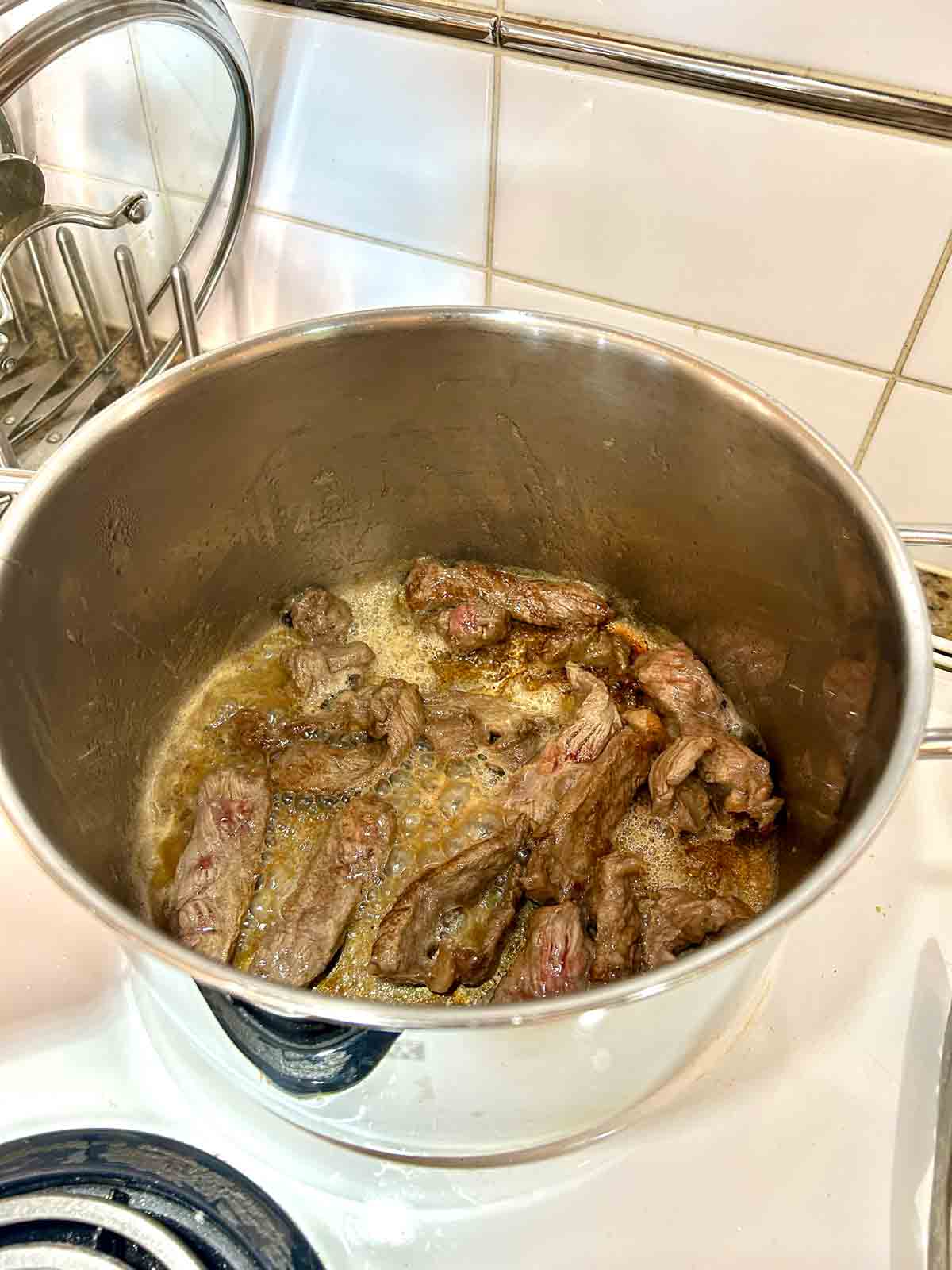 pieces of steak being seared in large pot.