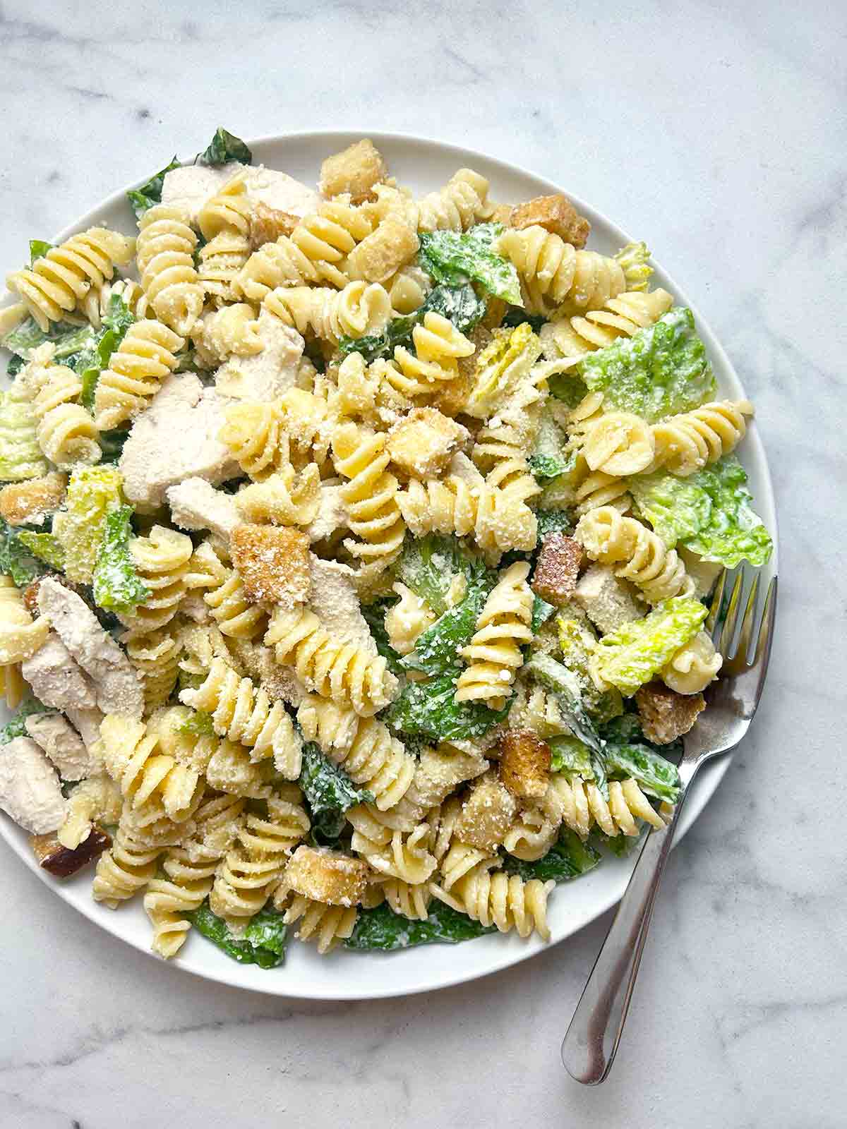 overhead shot of chicken caesar pasta salad on plate with fork.