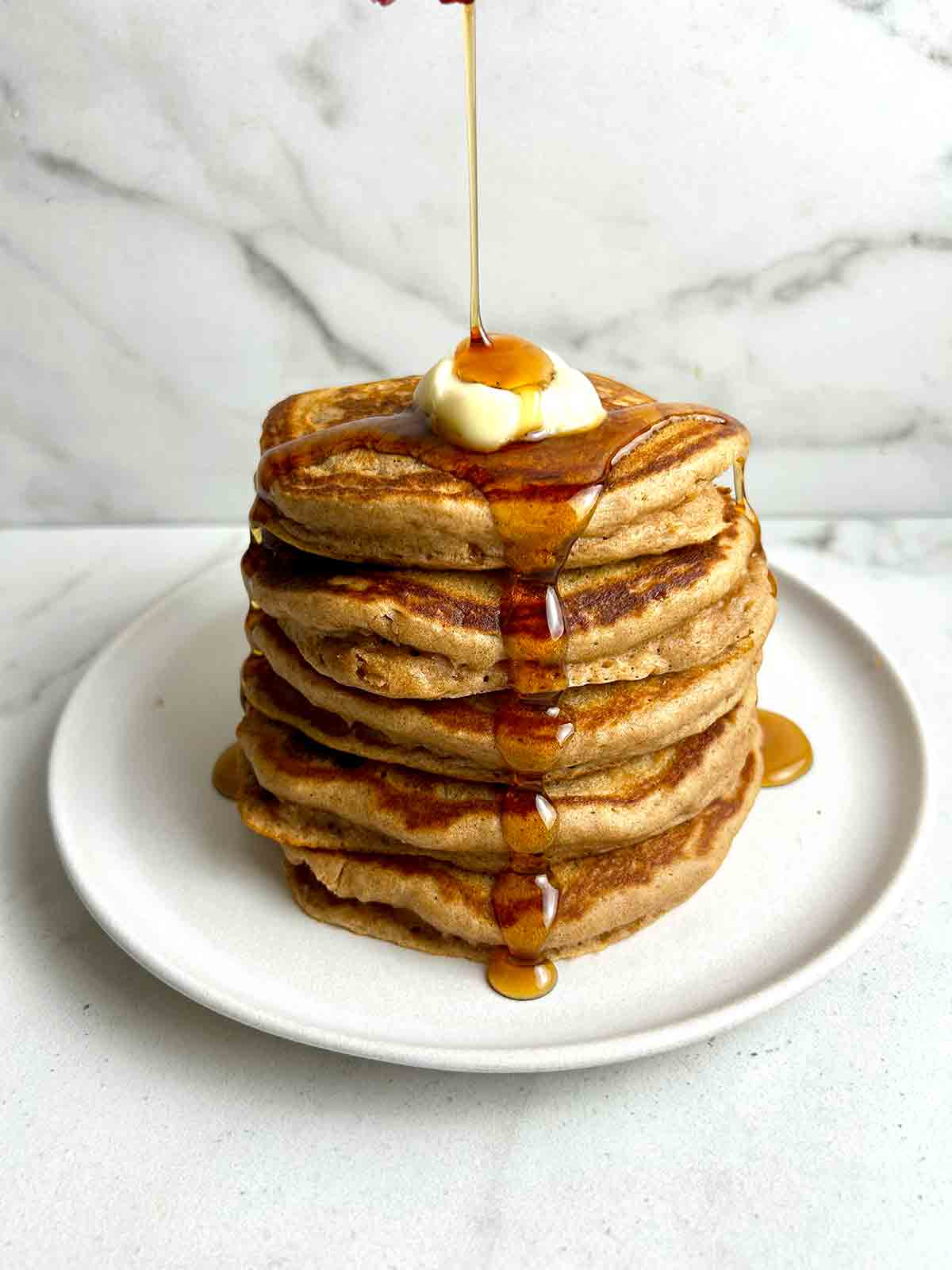 maple syrup being poured on stack of cinnamon brown sugar pancakes.