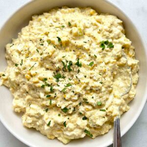 bowl of egg salad with chopped parsley and black pepper on top.
