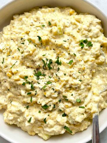 bowl of egg salad with chopped parsley and black pepper on top.