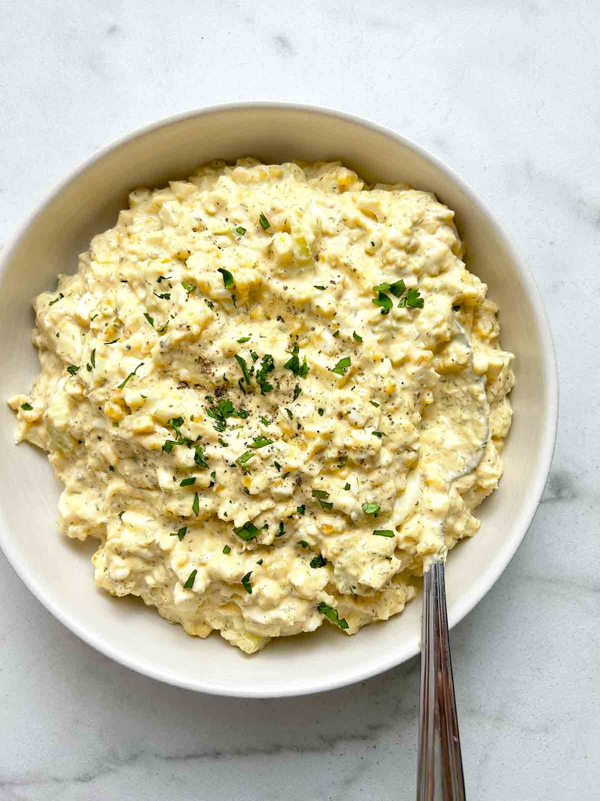 bowl of egg salad with chopped parsley and black pepper on top.
