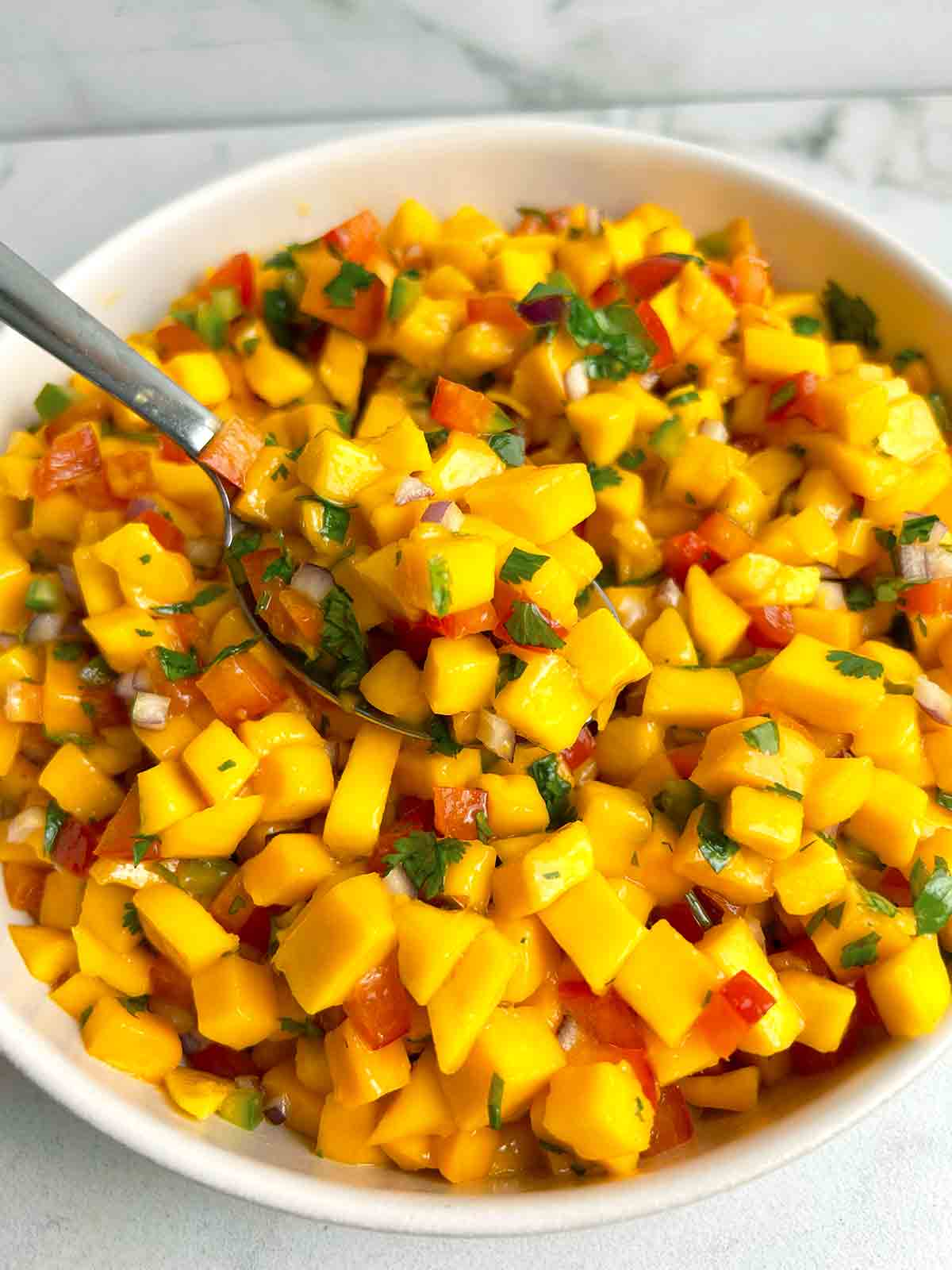 spoon lifting salsa from bowl of mango salsa.