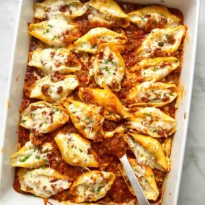 overhead shot of spoon lifting stuffed shells from casserole dish.