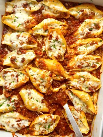 overhead shot of spoon lifting stuffed shells from casserole dish.