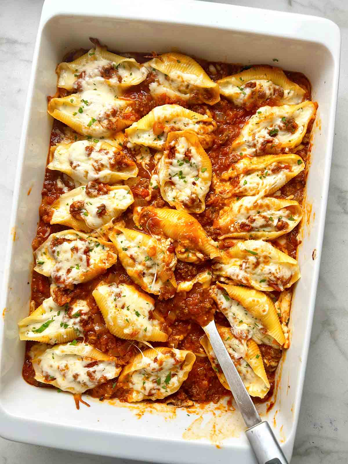 overhead shot of spoon lifting stuffed shells from casserole dish.
