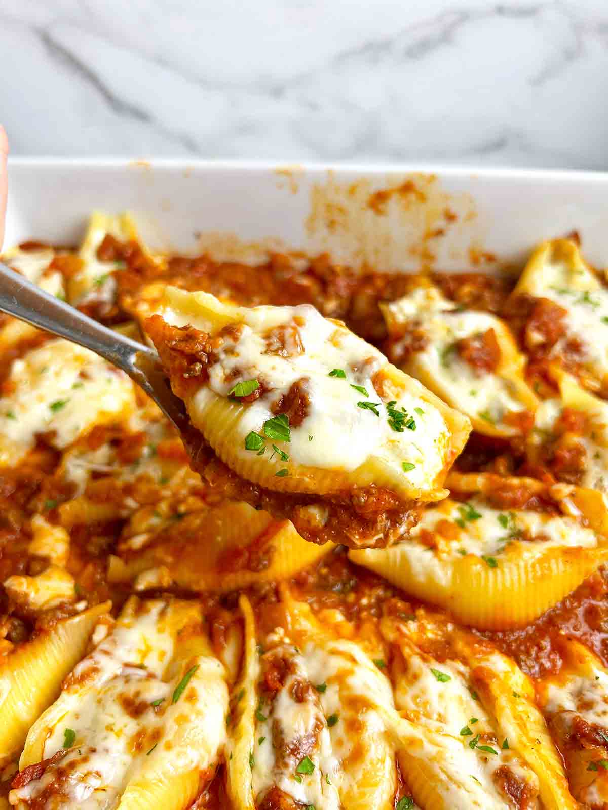spoon lifting stuffed shell from casserole dish.