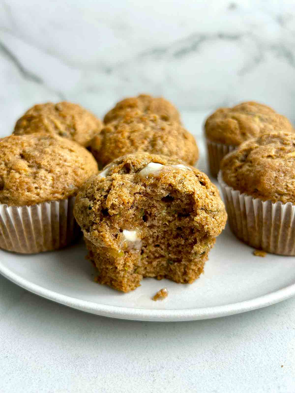 close up of zucchini muffin with bite taken out of it and some butter melting on top.