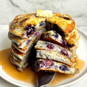 close up of stack of blueberry pancakes cut down the middle.
