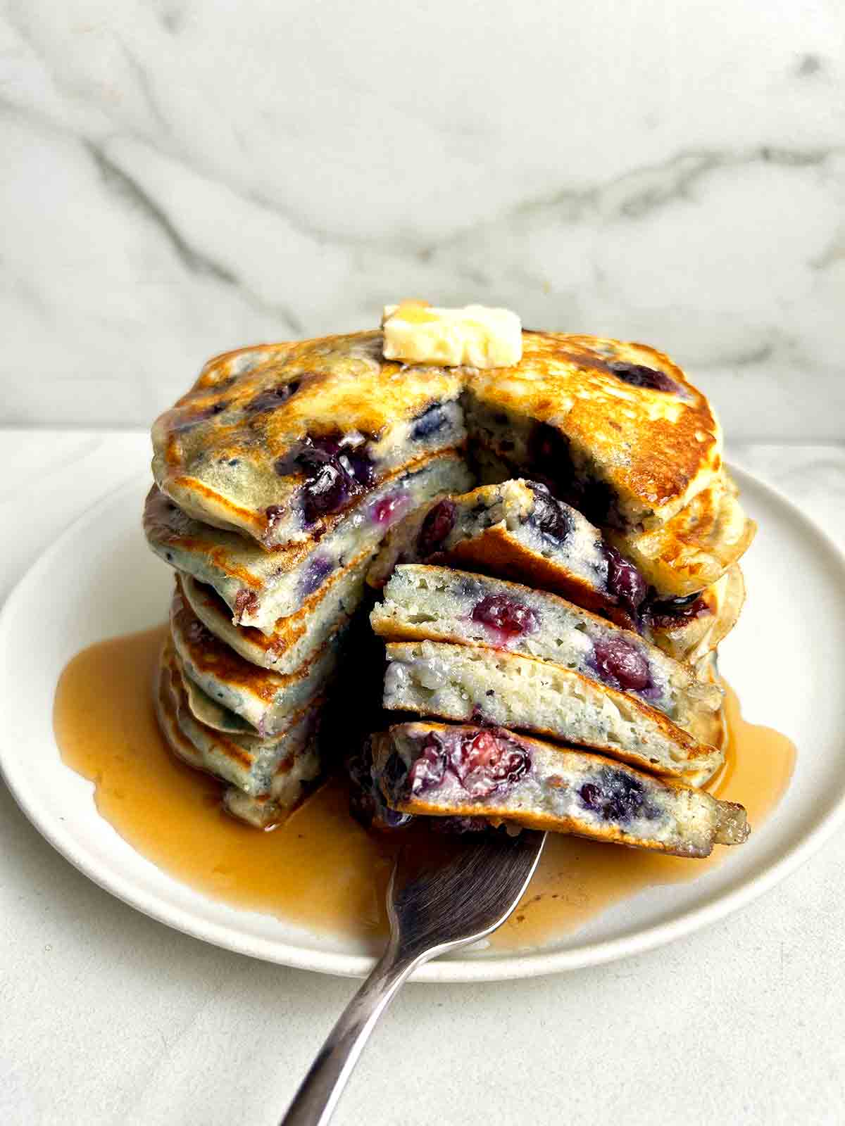 close up of stack of blueberry pancakes cut down the middle.
