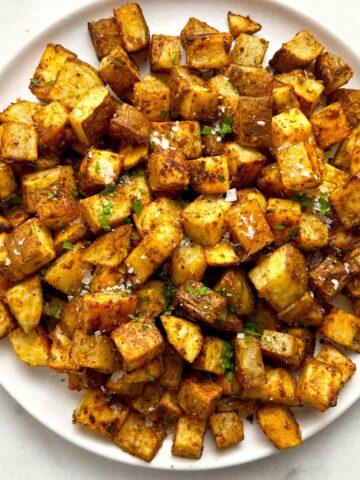 close up of bakes breakfast potatoes on plate; chopped parsley and flakey salt garnishing.