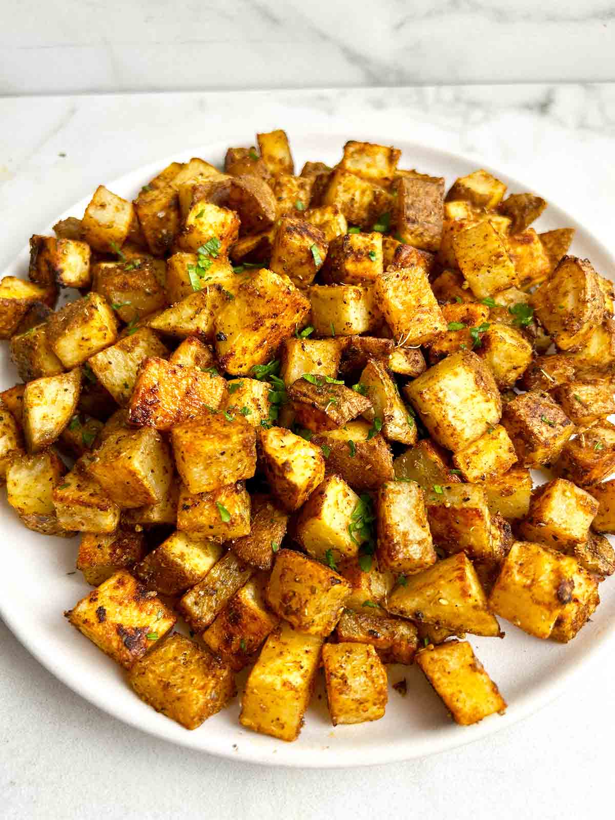 close up of bakes breakfast potatoes on plate; chopped parsley garnishing.