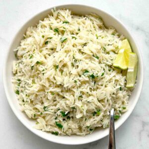 bowl of cilantro lime rice with sliced limes and spoon.