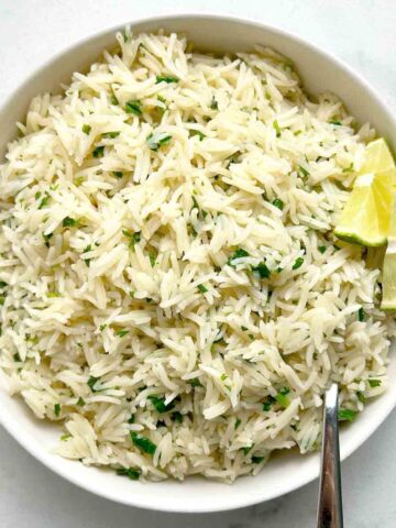bowl of cilantro lime rice with sliced limes and spoon.
