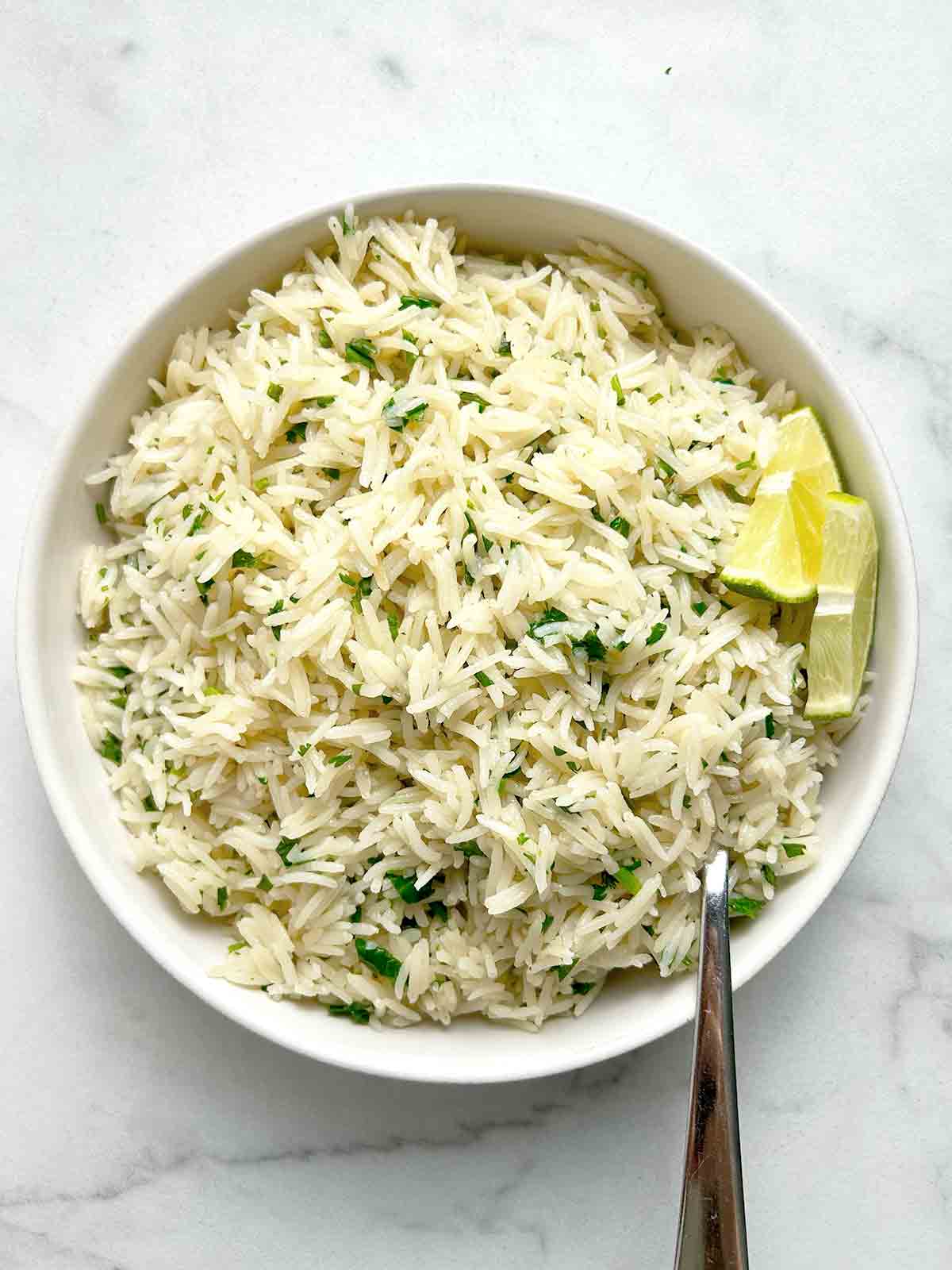 bowl of cilantro lime rice with sliced limes and spoon.