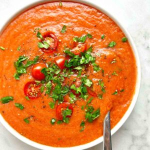 bowl of gazpacho soup with cherry tomatoes and chopped parsley on top.