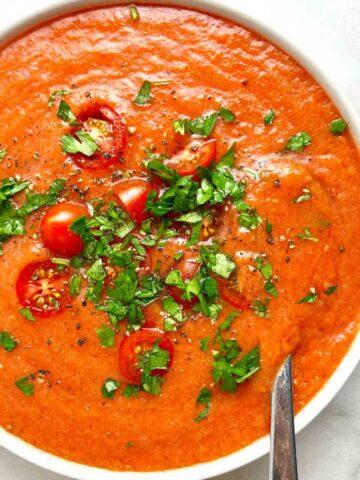 bowl of gazpacho soup with cherry tomatoes and chopped parsley on top.