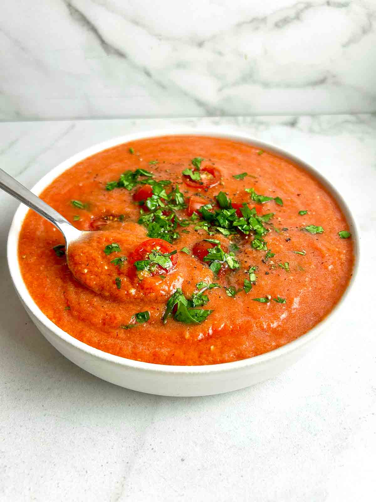 bowl of gazpacho soup with cherry tomatoes and chopped parsley on top.