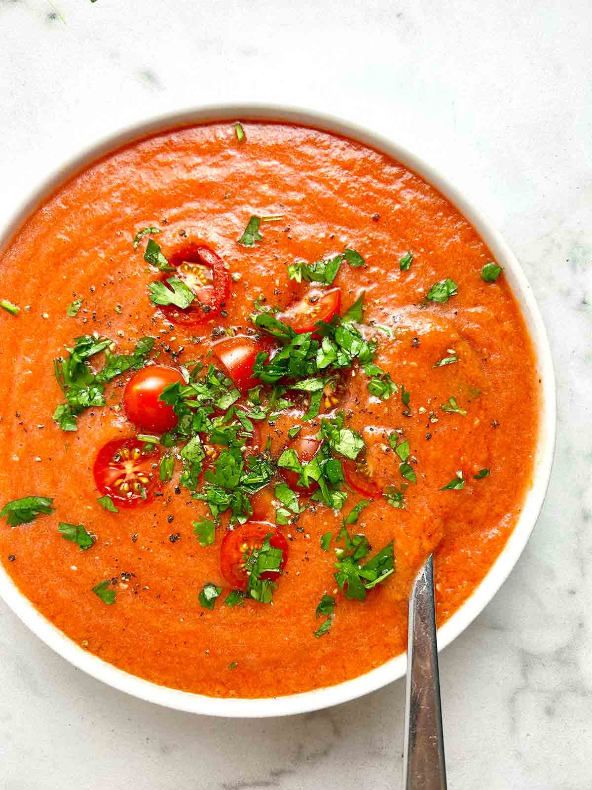 bowl of gazpacho soup with cherry tomatoes and chopped parsley on top.