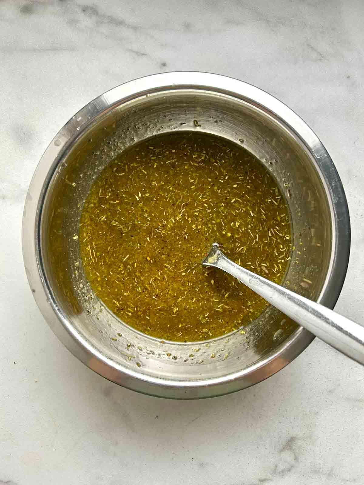 dressing whisked in small metal bowl with spoon.